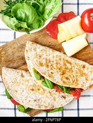 Piadina Romagnola mit Mozzarella-Käse, Tomaten, Schinken und Rucola-Salat auf einem Schneidebrett. Italienisches Fladenbrot oder offenes Sandwich. Selektiver Fokus. Stockfoto