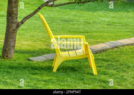 Gelber Stuhl auf grünem Rasen in einem Baumschatten Stockfoto