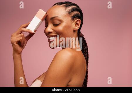 Hübsches Weibchen mit Beauty-Produkt. Frau lächelt mit geschlossenen Augen und hält ein kosmetisches Produkt. Stockfoto