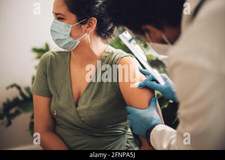 Arzt, der einen Arm der Frau mit Alkoholtupfen vorpreßt. Frau, die ihren Arm wegen ihres Covid-Impfstoffs desinfiziert hat. Stockfoto