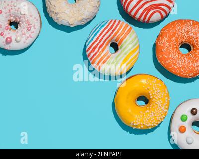 Köstliche glasierte Donuts auf blauem Hintergrund. Flat Lay - Set aus verschiedenen bunten Donuts oder Donuts auf blau mit Copy Space Rand. Helles Sonnenlicht mit harten Schatten Stockfoto