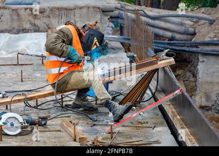 Ein Schweißer, der Schutzkleidung, Schutzhelm und Handschuhe trägt, schweißt Metallbalken, Eisenstangen und Strukturen im Arbeitsbereich. Stockfoto