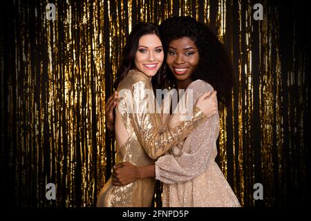 Foto von zwei charmanten Damen umarmen Blick Kamera toothy glänzend Lächeln tragen glänzende Kleider isoliert Lametta Hintergrund Stockfoto