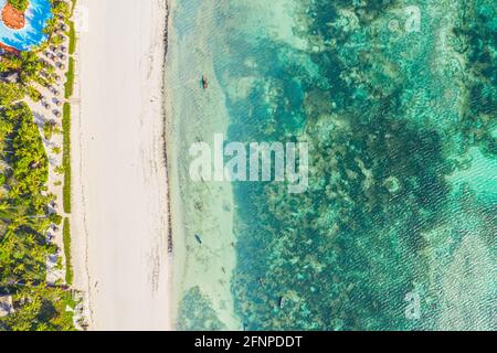 Luftaufnahme von Sonnenschirmen, Palmen am Sandstrand des Indischen Ozeans bei Sonnenuntergang. Sommer in Sansibar, Afrika. Tropische Landschaft mit Palmen, Sonnenschirme Stockfoto