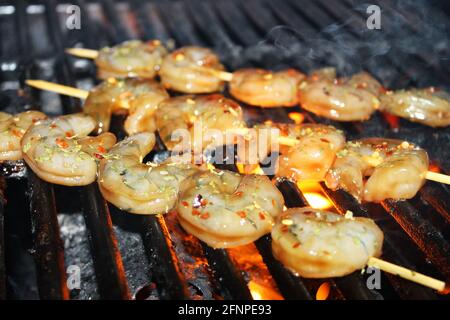 Nahaufnahme von glasierten und erfahrenen Garnelen auf Spiessen, die auf einem Grill gegrillt werden. Stockfoto