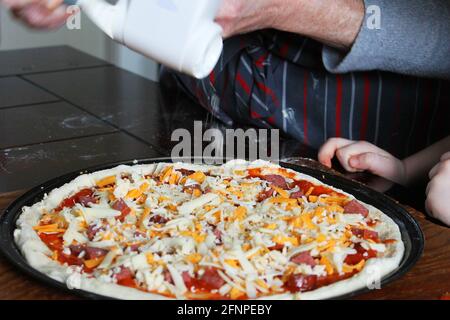 Nahaufnahme einer Frau und eines kleinen Kindes, die hausgemachte Pizza zubereiten. Hände nur im Rahmen. Stockfoto