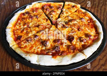 Nahaufnahme von frisch gebackener, hausgemachter Pizza, immer noch in der Pfanne, auf Holzschneidebrett. Stockfoto