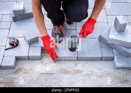 Der Meister in gelben Handschuhen legt Pflastersteine Stockfoto