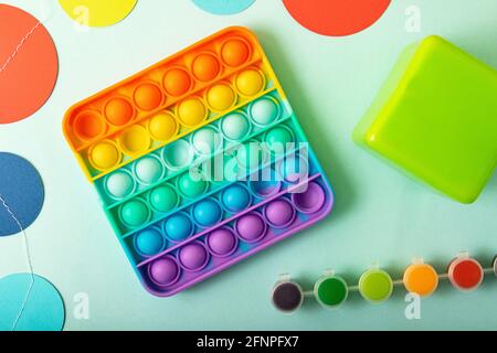 Draufsicht auf das neue Sinnesspielzeug - Rainbow Pop it mit Kinderspielzeug an den Seiten.Antistress-Spielzeug für Kinder und Erwachsene. Stockfoto