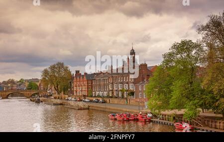 Blick auf den Fluss mit Gebäuden am Wasser und einer Brücke in der Ferne. Im Vordergrund stehen kleine Boote und oben ein wolkiger Himmel. Stockfoto