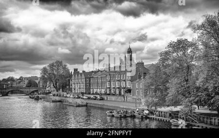 Blick auf den Fluss mit Gebäuden am Wasser und einer Brücke in der Ferne. Im Vordergrund stehen kleine Boote und oben ein wolkiger Himmel. Stockfoto