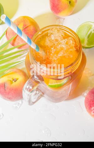 Kaltes Erfrischungsgetränk im Sommer, traditioneller Eistee-Pfirsich-Tee-Cocktail mit zerstoßenem Eis, Pfirsichscheiben und Zitrone auf hellem, trendigen, sonnigen gelben Hintergrund Stockfoto