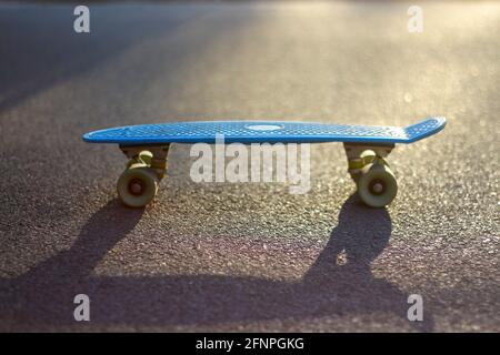 Unschärfe-Nahaufnahme blaues Penny-Brett auf der Asphaltstraße in der Sonne draußen. Unscharfes Bokeh. Mini-Cruiser. Sportkonzept. Skateboard steht im Stockfoto