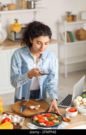 Junge Frau fotografiert leckere Pizza in der Küche Stockfoto