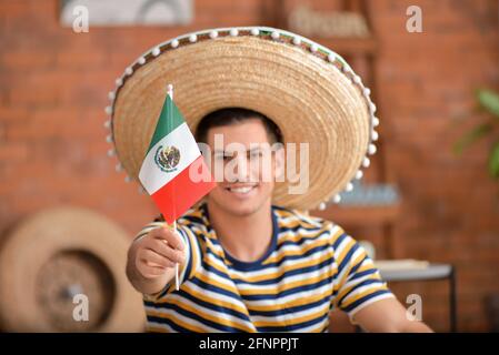 Gutaussehender Mann in Sombrero-Hut mit mexikanischer Flagge zu Hause Stockfoto