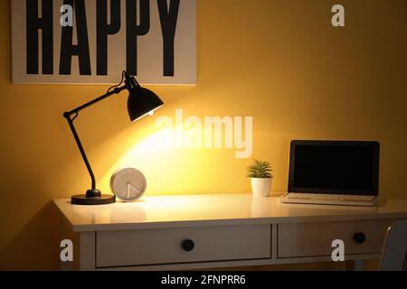 Leuchtende Lampe auf dem Tisch in der Nähe der Farbwand Stockfoto