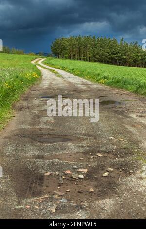 Weg zum Sturm. Dunkle Sturmwolken und unbefestigte Straße in Tschechien. Frühling stürmisches Wetter in der tschechischen Landschaft. Stockfoto