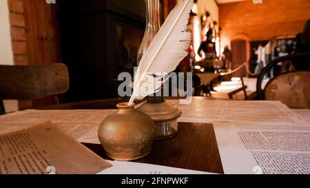 Weiße Federkiel und Tintenfass im alten Universitätsaula. Auf dem Tisch befinden sich Buchstaben. Mittelalterliche Atmosphäre Stockfoto