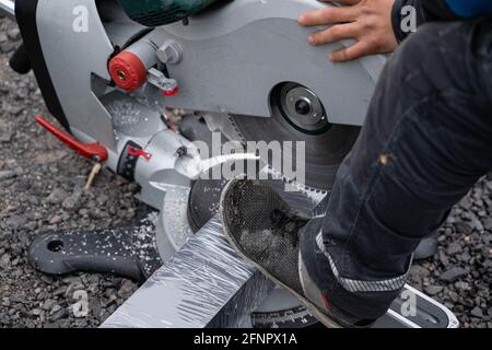 Mann schneidet großes Stück Aluminium mit elektrischer Kreissäge Stockfoto