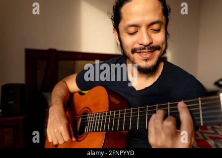 Junger latein, der zu Hause im Schlafzimmer Gitarre spielt Stockfoto