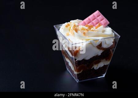 Kleinigkeit aus Schokoladenkeks mit Karamell-Erdnussfüllung auf schwarzem Hintergrund. Das Dessert ist mit cremiger Käsecreme und rosafarbener Schokolade dekoriert. Stockfoto