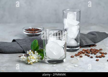 Eiswürfel mit klaren Gläsern auf grauem Hintergrund mit Kaffeebohnen. Zubereitung von Getränken. Stockfoto