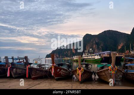 Bei Ebbe auf der Tonsai Bay in der Morgendämmerung, Kho Phi Phi, Thailand, verankerte Longtail-Boote mit gefesselten Stücken farbigen Seidentuchs auf ihren Bögen Stockfoto