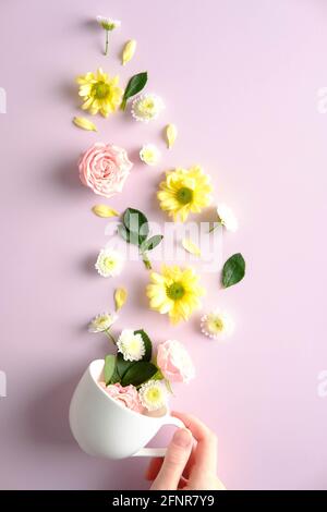 Weibliche Hand hält Tee Tasse mit Blumen auf pnik Hintergrund. Kreative, flache Lay-Komposition, Draufsicht. Stockfoto