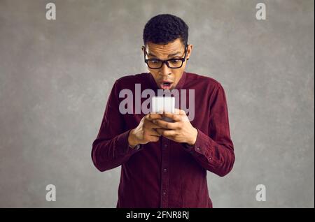Überrascht afro amerikanischer Mann mit offenem Mund Blick auf Telefon Aufnahme im Studio Stockfoto