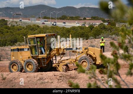 Ein Schwermaschinen-Betreiber verwendet einen Caterpillar 120H Motorgrader, um Schmutz auf einer Baustelle im Straßenbau in Santa Fe, New Mexico, zu transportieren. Stockfoto