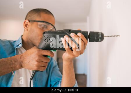 Junger Mann mit einem elektrischen Bohrer und Loch in der Wand. Stockfoto