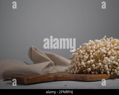 Frischer goldener Nadelpilz oder Enoki-Pilze, auf hölzernem Schneidebrett auf grauem Betongrund Stockfoto