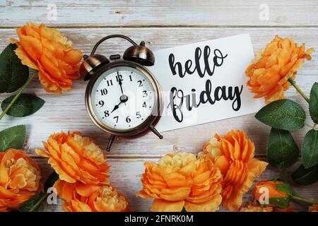 Hello Friday-Karte und Wecker mit orangefarbener Blumendekoration auf hölzernem Hintergrund Stockfoto