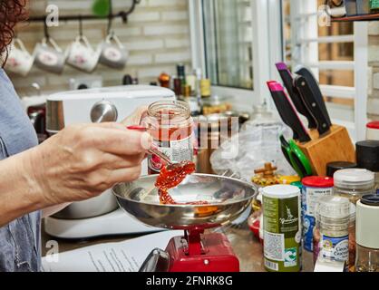 Israel, Rishon LeZion - 8. Mai 2021: Frau wiegt sonnengetrocknete Tomaten auf einer Waage, um sonnengetrocknete Tomatenmuffins zu machen. Stockfoto