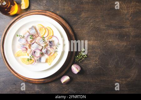 Gesalzener Hering mit Gewürzen, Kräutern und Zwiebel auf Teller auf Holzboden mit Kopierfläche. Marinierter Fisch in Scheiben. Essen mit gesunden ungesättigten Fetten, O Stockfoto