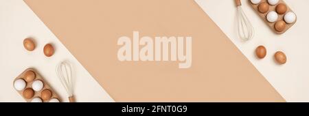 Banner mit Eiern in Holzeierkasten und Schneebesen auf beigem Hintergrund. Flach liegend Draufsicht Kopierbereich. Stockfoto