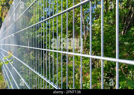 Grauer Gartenzaun aus Metall mit selektivem Fokus und einem verschwommenen Gartenhintergrund Stockfoto