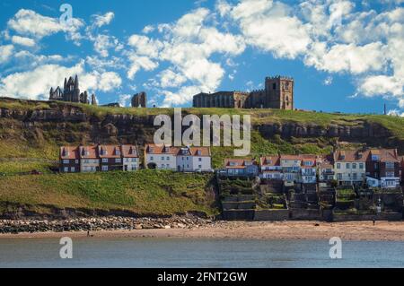 Die Ferienhäuser und der Strand der East Cliff in Whitby, mit Whitby Abbey und der Kirche St. Mary auf dem Hügel darüber. Stockfoto