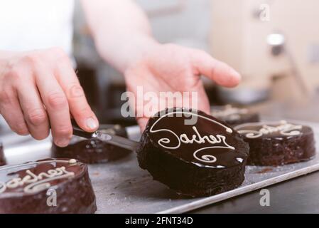 Hände halten Schokolade sacher Kuchen in der Bäckerei. Konditor Hände halten Kuchen in Konditorei Labor. Konzept der traditionellen handgefertigten sachertorte c Stockfoto