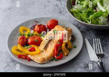 Gebackenes rotes Fischfilet Arctic Saibling auf einem Teller mit Gemüse, Salat in einer Schüssel mischen, leckeres herzhaftes gesundes Abendessen Stockfoto