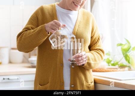 Nicht erkennbare Großmutter, die zu Hause Wasser in das Glas gießt Stockfoto