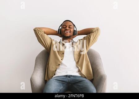 African Guy Listening Music Entspannendes Sitzen Im Sessel, Grauer Hintergrund Stockfoto