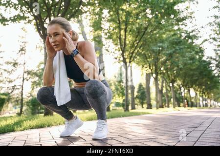 Tun Sie es für sich selbst. Müde, athletische Frau mittleren Alters in Sportkleidung, die wegschaut und sich während des Trainings im grünen Park an sonnigen Tagen ausruht Stockfoto