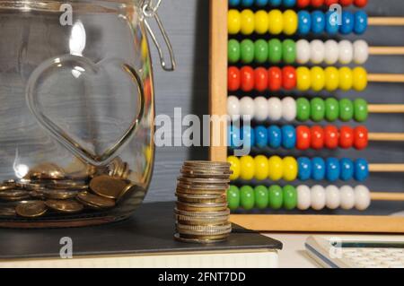 Stapel von Goldmünzen, Glas und bunten Abakus auf dem grauen Hintergrund - Geld sparen Stockfoto