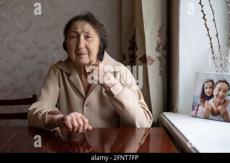 Sehr alte Frau mit Kopfhörern, die Videogespräche am Telefon zu Hause führt. Videogesprächs-Konzept. Headshot online. Stockfoto