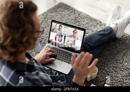 Junger Mann, der einen Latop-Computer benutzt, um mit seinem Geschäftsteam zu sprechen, winkt mit der Hand gegen die Webcam, spricht mit seinen Kollegen oder Freunden Stockfoto