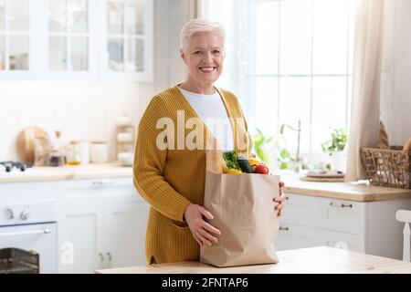 Lächelnde alte Frau mit Einkaufstasche, die im Internet bestellt wurde Stockfoto