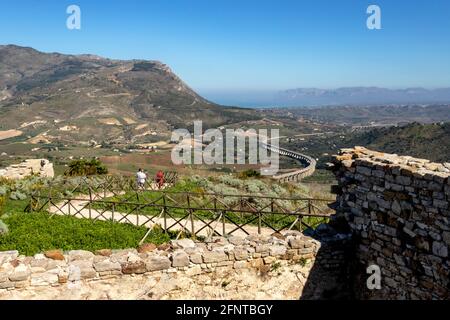 Touristen, die den Weg hinunter zum griechischen Theater von Segesta mit Blick auf die kurvenförmige Autobahn, die Autostrada A29, Trapani, Sizilien, Italien. Stockfoto