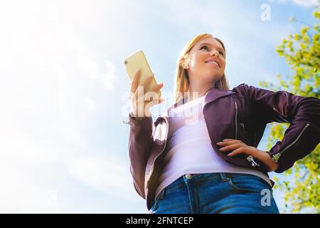 Junge schöne lächelnde Erwachsene kaukasischen Mädchen zu Fuß im Freien in der parken Sie mit Chat-Kommunikation mit kabellosen Kopfhörern mobile Lesung sprechen lis Stockfoto