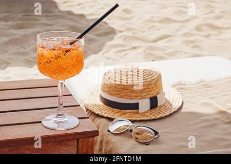 Ein Glas aperol Spritz, Strohhut und Sonnenbrille am Strand Stockfoto